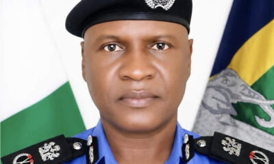 Portrait of a police officer in a blue uniform and black beret, with a flag in the background representing service and duty.
