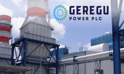 Industrial power plant with cooling towers and Geregu Power PLC logo in the sky above. We see blue steel frameworks and piping.