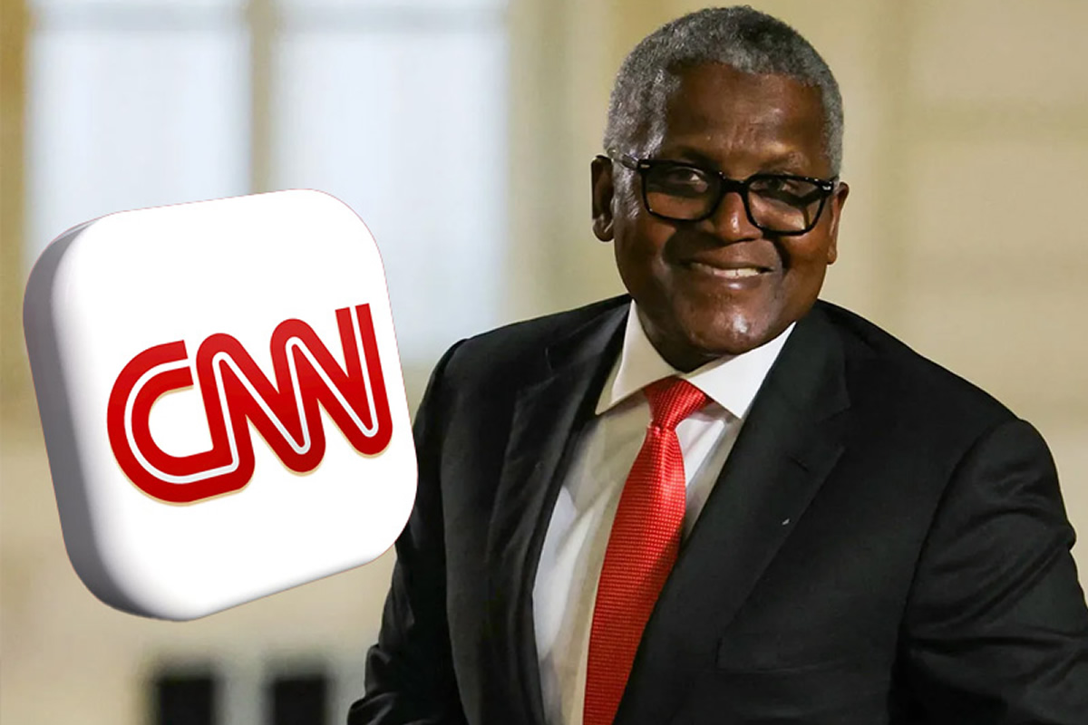 Smiling man in a dark suit and red tie with a large CNN logo foreground.