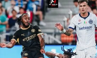 Two soccer players chase the ball during a match; one in black and gold kit, the other in a white pinstripe kit.