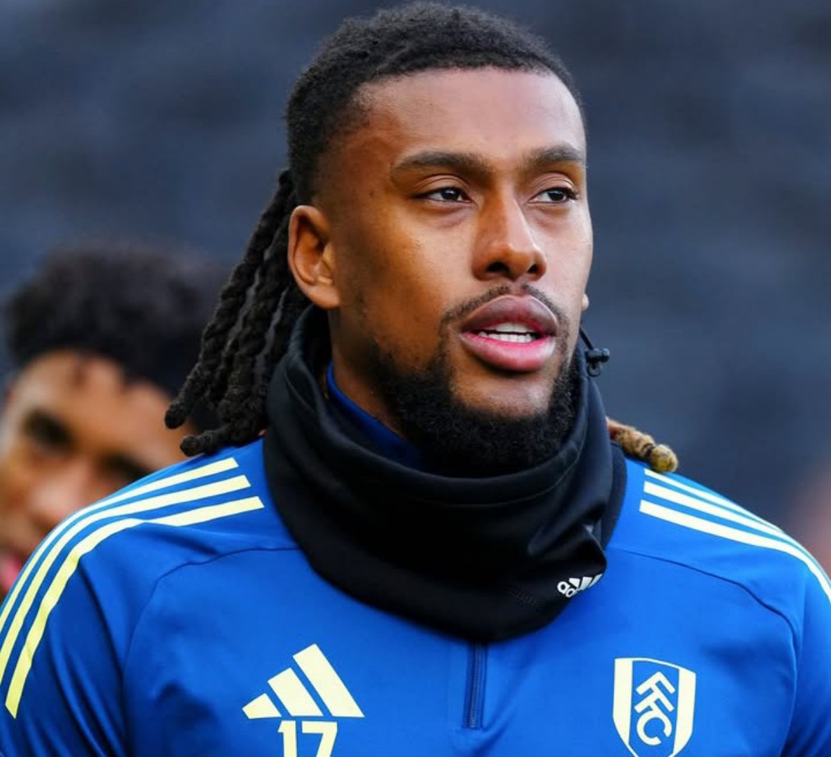Footballer in blue training jersey with crest and number 17, wearing a black neck warmer, outdoors during training.