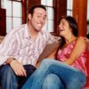 Smiling couple sitting close on a beige sofa, laughing together in a cozy living room setting.