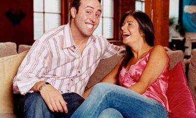 Smiling couple sitting close on a beige sofa, laughing together in a cozy living room setting.