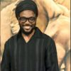 Smiling man with a black turban, black-framed glasses, and a black striped shirt posing in front of a warm, abstract backdrop.