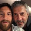 Two men smiling for a close-up selfie, faces side by side indoors.