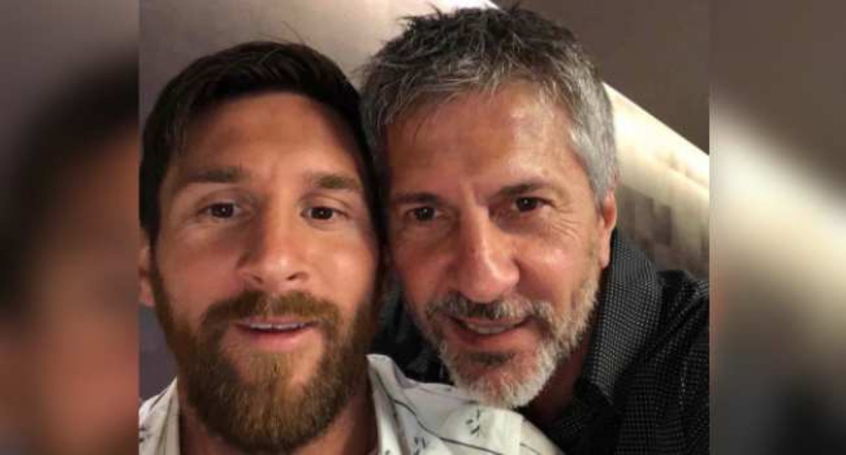 Two men smiling for a close-up selfie, faces side by side indoors.