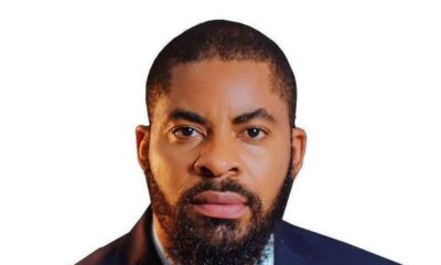 Professional headshot: man with a full beard in a navy suit and red tie against a white background