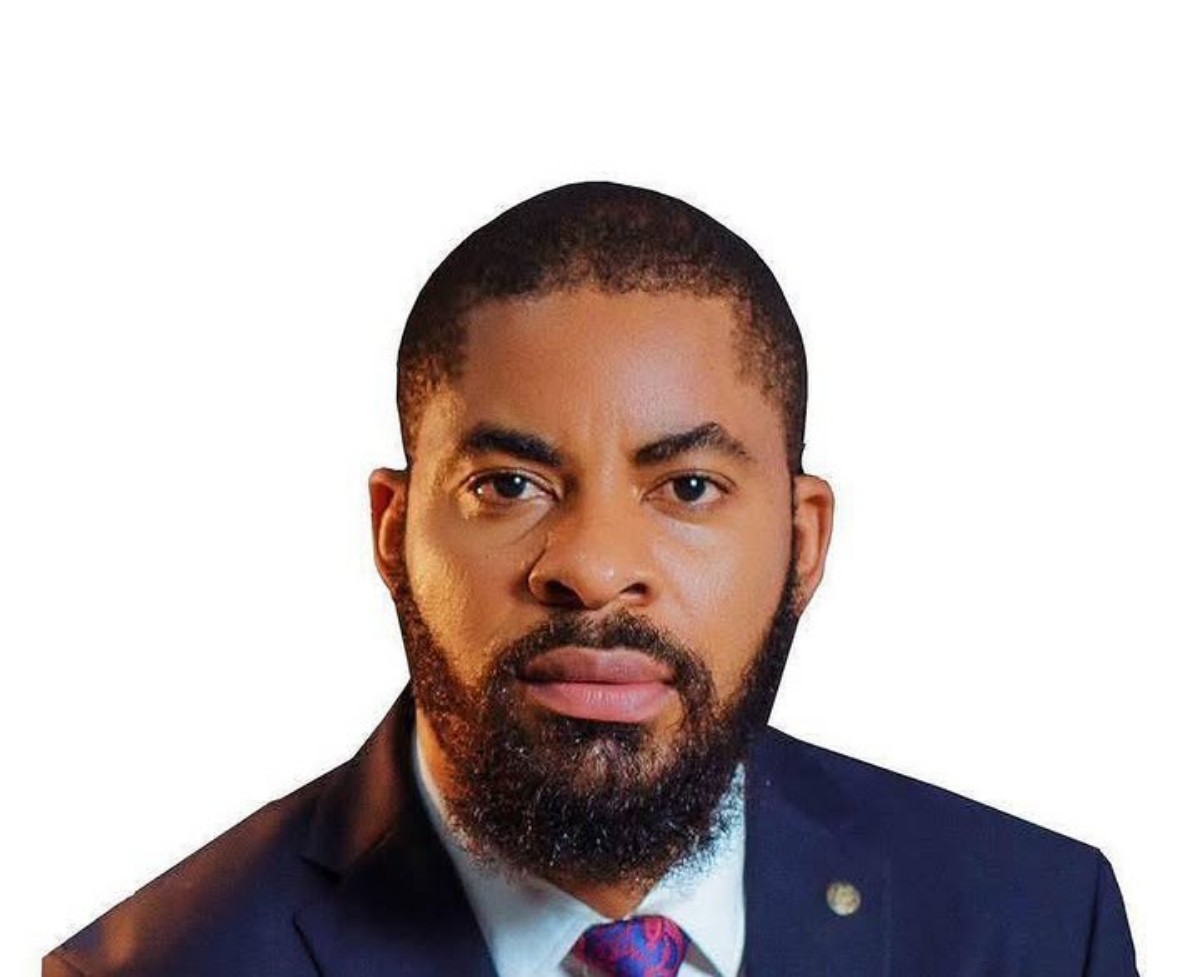 Professional headshot: man with a full beard in a navy suit and red tie against a white background