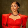 Elegant portrait of a woman in a red lace gown with a statement necklace, posed against a dark backdrop.
