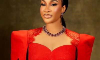 Elegant portrait of a woman in a red lace gown with a statement necklace, posed against a dark backdrop.
