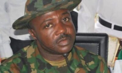 Nigerian soldier in camouflage uniform and cap, seated indoors, looking to the side.