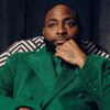 Portrait of a man in a green velvet suit, seated with chin resting on his hand, looking at the camera.