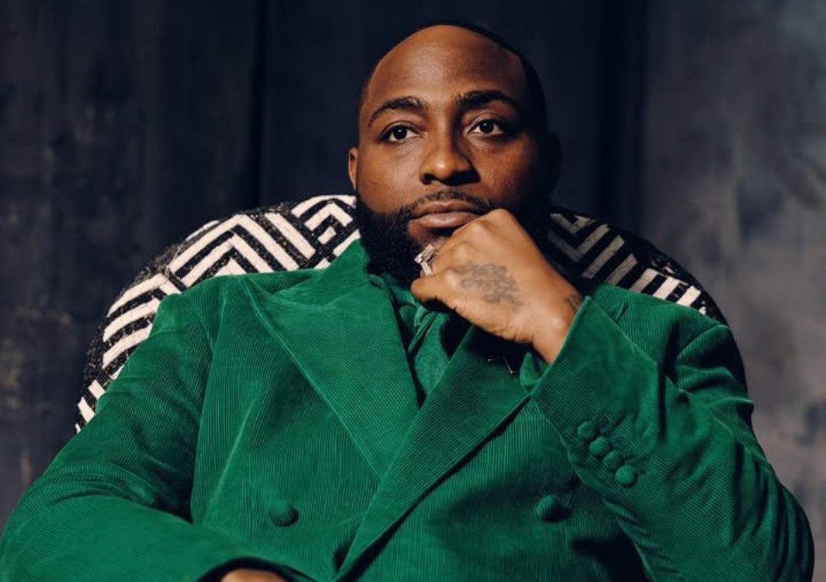 Portrait of a man in a green velvet suit, seated with chin resting on his hand, looking at the camera.