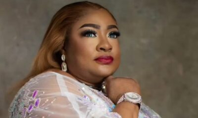 Portrait of a person with blonde hair wearing a sheer, bejeweled gown, large earrings, and a sparkling bracelet, resting chin on hand.
