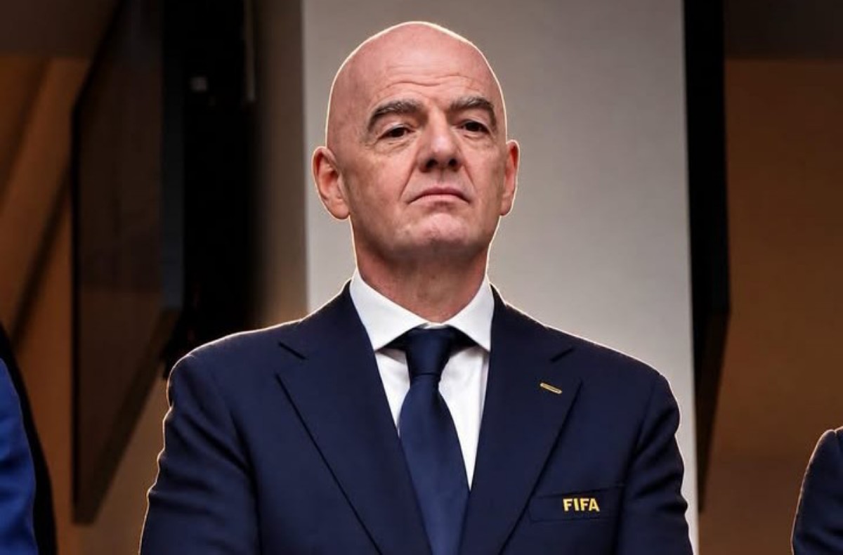 Bald man in a navy suit and blue tie with a FIFA emblem on the lapel, looking serious at a formal event