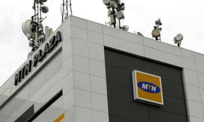Corner of a modern building with MTN logo on a dark panel and a cluster of satellite dishes and antennas on the roof, indicating a telecom facility