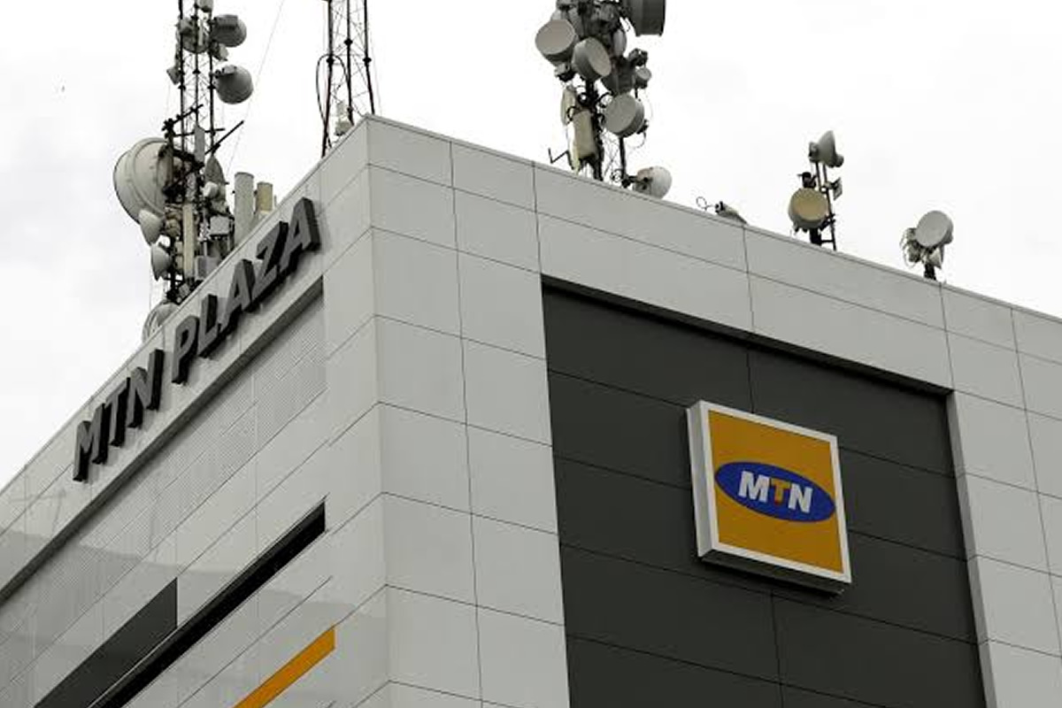 Corner of a modern building with MTN logo on a dark panel and a cluster of satellite dishes and antennas on the roof, indicating a telecom facility
