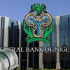 Facade of the Central Bank of Nigeria with its logo and a rolled bundle of US dollar bills in the foreground.