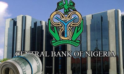 Facade of the Central Bank of Nigeria with its logo and a rolled bundle of US dollar bills in the foreground.