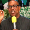 Man wearing glasses speaks into a yellow microphone, gesturing with his right hand during a formal event.