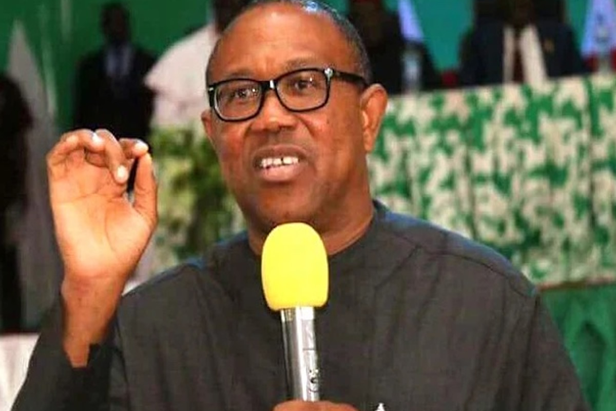 Man wearing glasses speaks into a yellow microphone, gesturing with his right hand during a formal event.