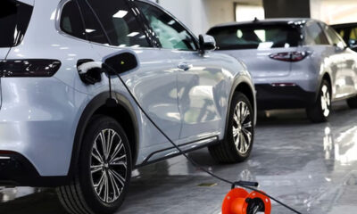 Electric SUV in a showroom plugged into a charging cable with other cars on display in the background.