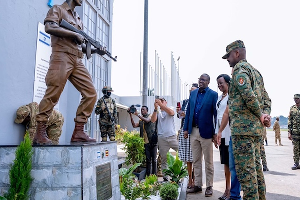 Soldiers guard a memorial as civilians observe a ceremony, with one person taking photos and others watching respectfully.