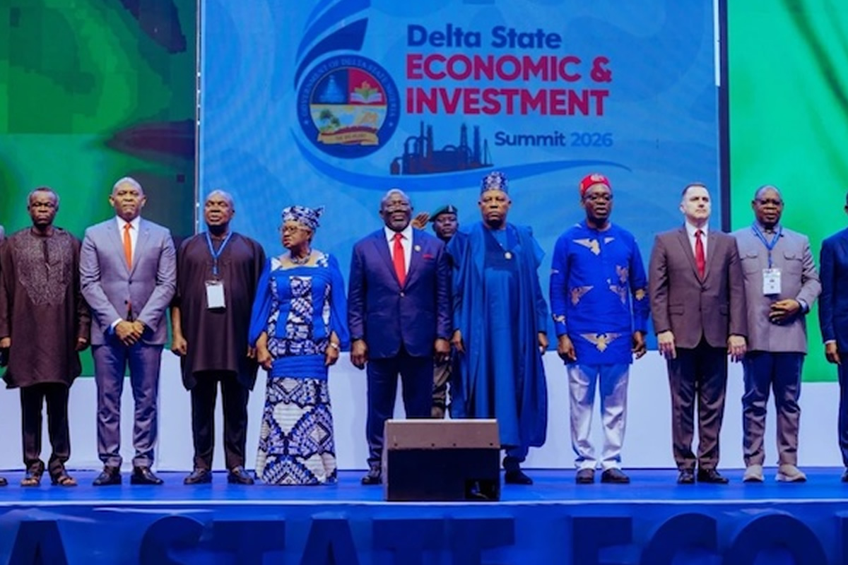 Group of officials on stage at the Delta State Economic & Investment Summit 2026, standing in a line with a blue event banner behind them.