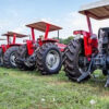 Row of red tractors with canopies parked on a grassy field.