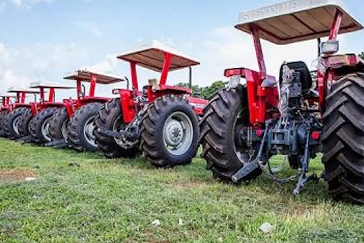 Row of red tractors with canopies parked on a grassy field.