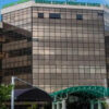 Glass-front office building with reflective panels and a green arched walkway to the entrance.