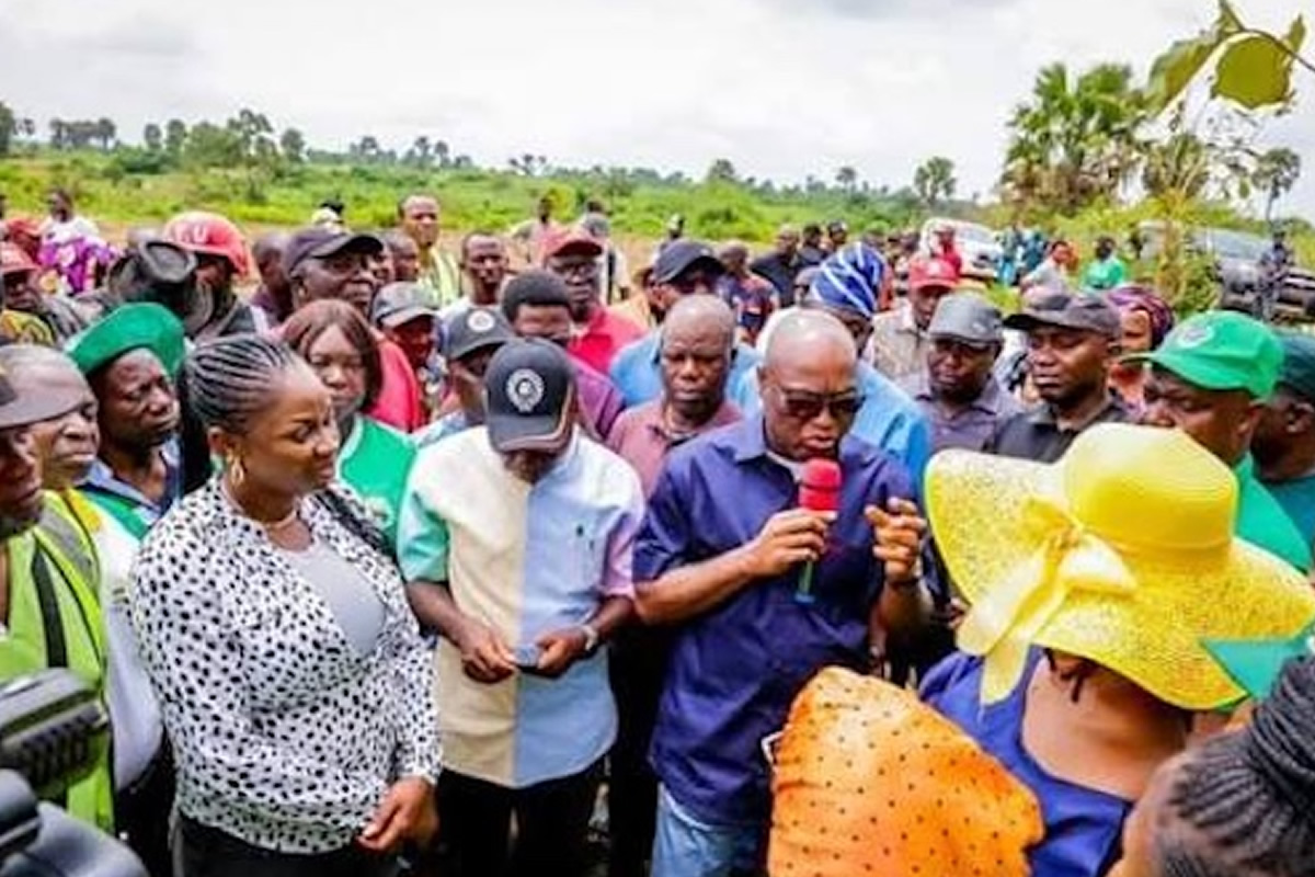 Man in a dark blue shirt speaks into a red microphone to a crowd at an outdoor community gathering.