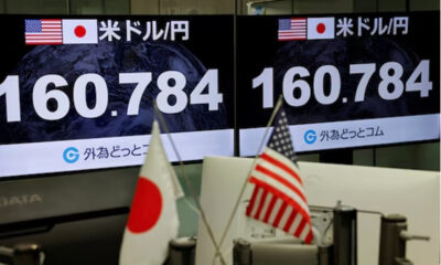 Two large screens show the USD/JPY exchange rate with US and Japan flags, foregrounded by desk flags (US and Japan).