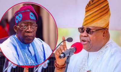 Man in white agbada and gold-striped hat speaks into a red microphone; an inset shows an older man in blue attire and cap.