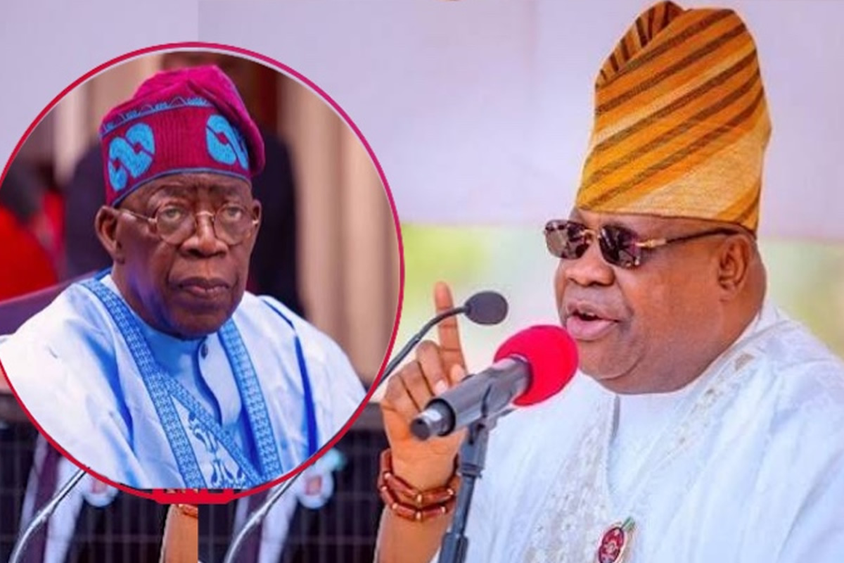 Man in white agbada and gold-striped hat speaks into a red microphone; an inset shows an older man in blue attire and cap.