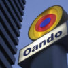 Oando company sign with a circular yellow-red-blue logo against a blue sky