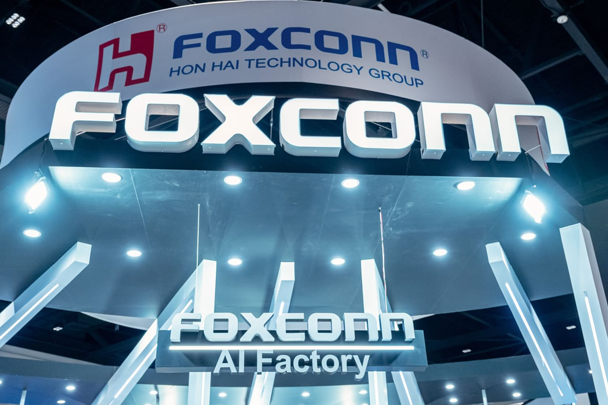 Foxconn booth signage at a tech expo with a large 'FOXCONN' logo and nearby 'AI Factory' text under bright lighting.