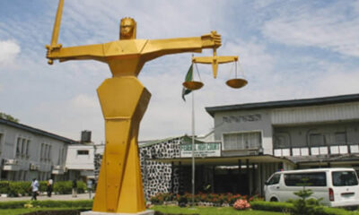 Golden statue of a muscular figure holding scales of justice in a public plaza outside a building