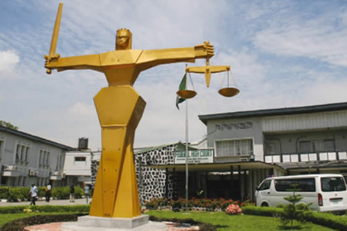 Golden statue of a muscular figure holding scales of justice in a public plaza outside a building