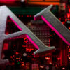 Close-up of large gray metal letters forming 'AI' on a red-lit computer motherboard.