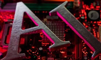 Close-up of large gray metal letters forming 'AI' on a red-lit computer motherboard.