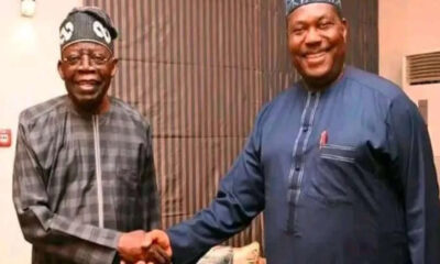 Two smiling men in traditional West African attire shake hands indoors.