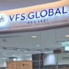 Sign reads 'VFS Global' with logo and the slogan 'Partnering Governments. Providing Solutions.' inside a modern office lobby.
