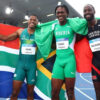 Three male sprinters on a track celebrate with national flags draped over their shoulders (South Africa, Nigeria, Trinidad & Tobago).